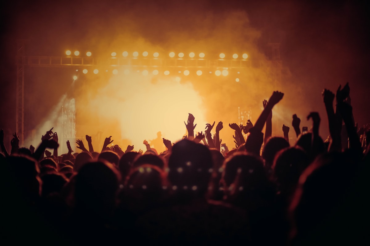 Crowd in front of a bright stage wash with rigging overhead.
