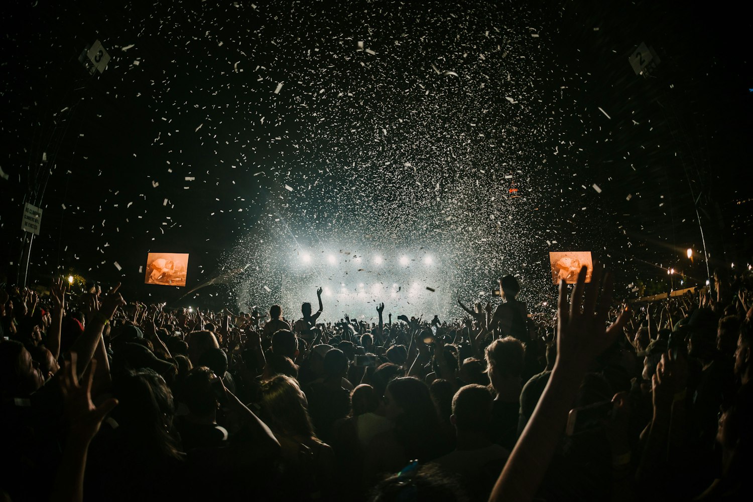 Stage lighting and haze over a festival audience with rigging overhead.